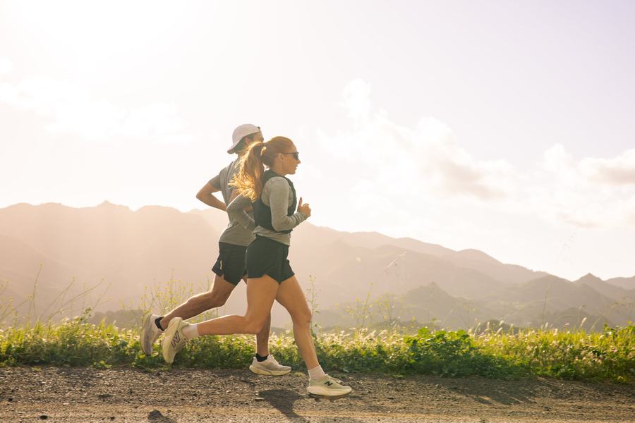 Two runners on a ridge trail, backlit, mountains behind