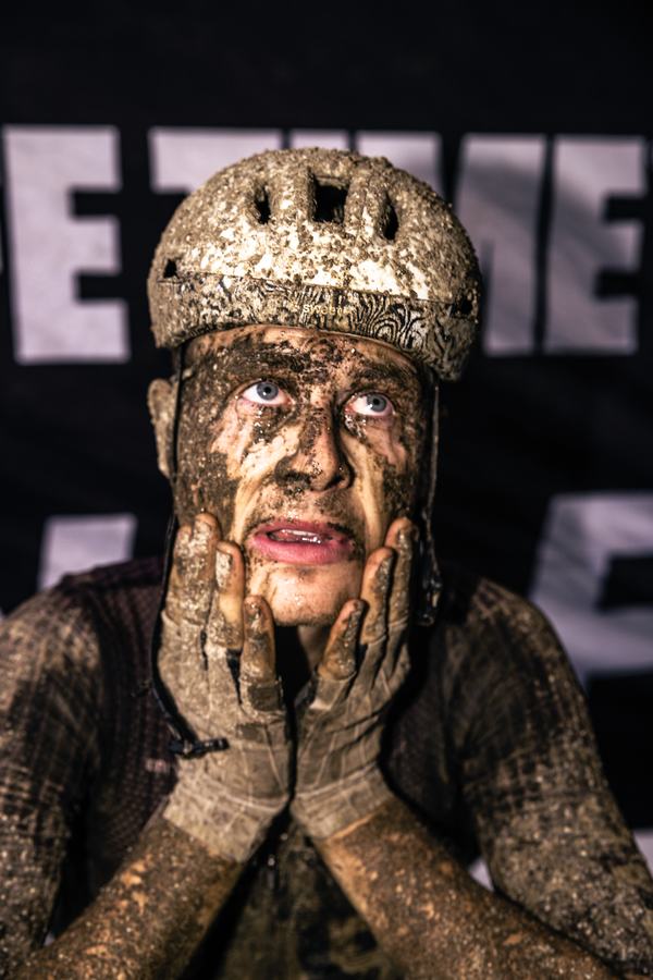 Mud-covered rider, hands to face, at the finish